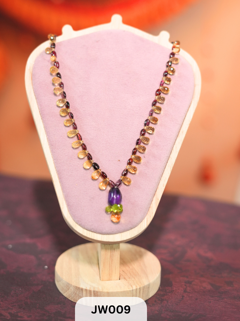 The necklace features a vibrant mix of briolette-cut semi-precious gemstones, including amethyst, peridot, citrine, and garnet Travel Story Collectives