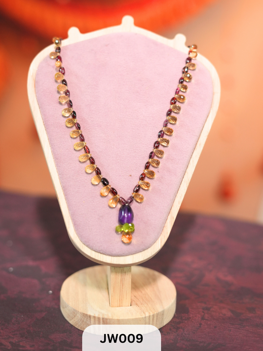 The necklace features a vibrant mix of briolette-cut semi-precious gemstones, including amethyst, peridot, citrine, and garnet Travel Story Collectives